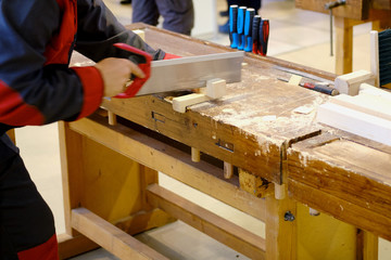 A carpenter cuts a piece of a wooden bar on a workbench with a saw