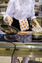 Woman chef roasts in a frying pan in the hotel's public kitchen