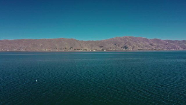 Aerial drone shot zoom out of Lake Sevan and seagulls flying on background of Mount Ararat. Aerial drone zoom out shot of Lake Sevan under bright blue sky