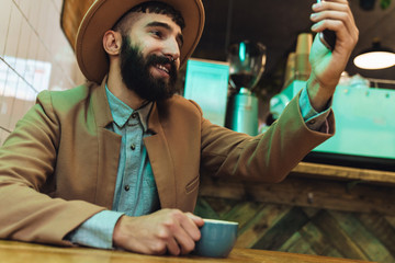 Fototapeta na wymiar Image of attractive young man wearing hat using cellphone in cafe