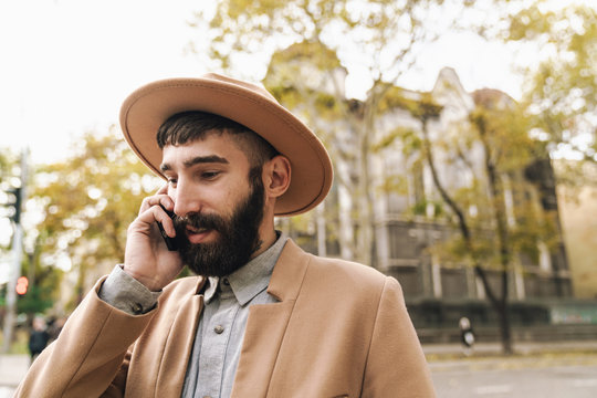 Image of stylish young man talking on cellphone while walking outdoors
