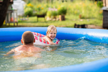 happy family, dad, father and daughter 4 years old in a rubber ring swim in an inflatable pool, laugh fun, vacation in the village