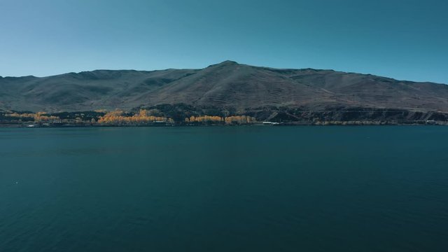 Aerial drone shot zoom in of Lake Sevan and seagulls flying on background of Mount Ararat. Aerial drone zoom out shot of Lake Sevan under bright blue sky