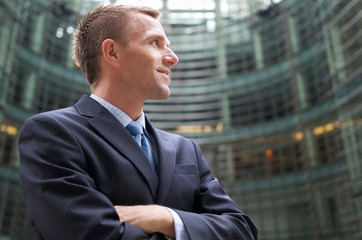 Confident businessman standing outside an office building smiling in dark pinstripe suit