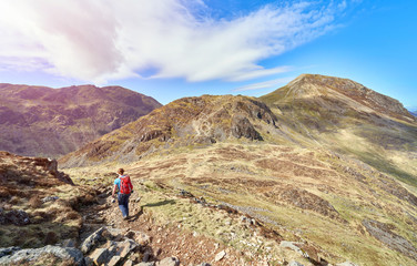 A hiker descending the summit of Hay Stacks and walking towards Seat and High Crag with views of Pillar to the Left on a sunny day in the English Lake District.