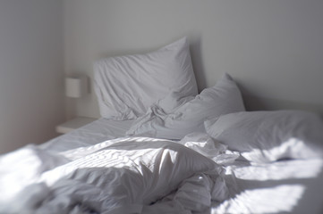Tilt-shift view of morning sun streaming across rumpled sheets and dented pillows of a well...