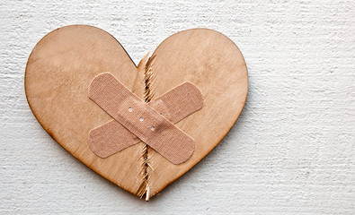 Two parts of broken wooden heart taped by a patch. Concept of the forgiveness, renewal of relations...