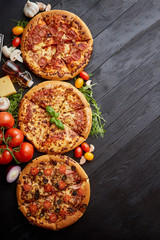 Freshly served, three various pizzas placed among tasty ingredients. Top view