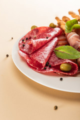 close up view of delicious meat platter served with olives and breadsticks on plate on beige background
