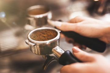 Barista woman holding coffee holder with ground coffee near professional coffee machine close up