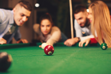 Group of friends play billiards at night out