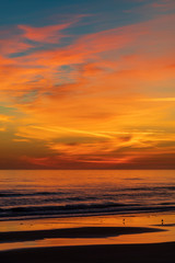 Fototapeta na wymiar Vertical image of a sunrise before the sun rises above the horizon along the Atlantic Coast of Port Orange, Florida illuminating the clouds above and the sea below. 