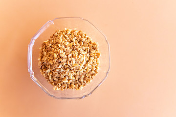 Glass bowl of roasted crushed peanuts isolated on table background.