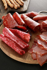 delicious meat platter on wooden board on black surface