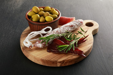 delicious meat platter served with olives on board on black surface