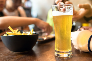 Beer in a tall glass on table with a group of friends is spending time together in cafe.