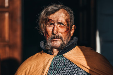 Portrait of a medieval senior warrior man in armor after a battle with dirty and blood-smeared face