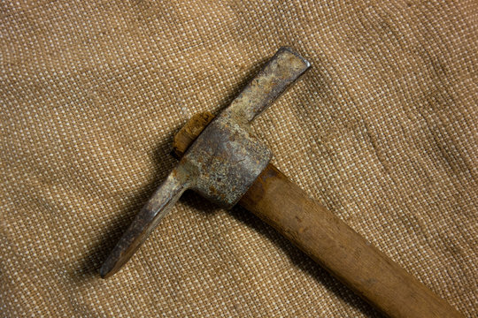 Miner hammer like pickaxe or mattock on bagging fabric background. Closeup view of rustic old hand tool for hard working to extract fossils or concept of block chain currency mining