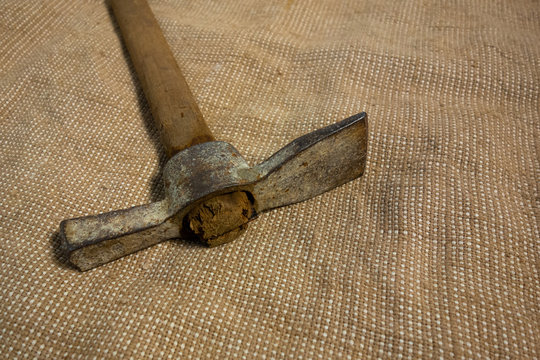 Miner hammer like pickaxe or mattock on bagging fabric background. Closeup view of rustic old hand tool for hard working to extract fossils or concept of block chain currency mining