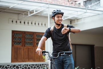 asian young man standing with folding bike while looking her watch in front the house building