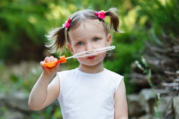 Portrait of a cute little girl on the background of nature. She blows air bubbles.
