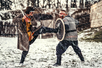 Two ancient warriors in armor with weapons fighting with swords in the snow