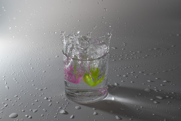 Colorful cubes dropped in a glass full of water, making beautiful splashes and wetting the table