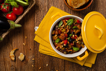 Traditional Italian caponata, served with croutons in a yellow, sunny pot. Decorated with basil and...