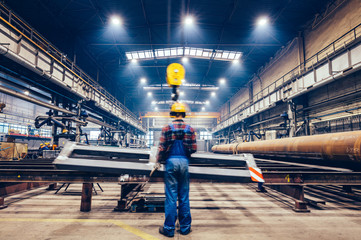Blue-collar worker operating crane hook in a big factory.