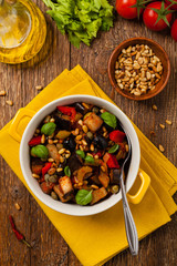 Traditional Italian caponata, served with croutons in a yellow, sunny pot. Decorated with basil and pine nuts.