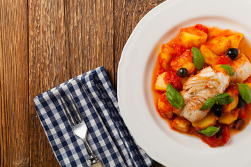 Traditionally prepared cod in Spanish. Served in tomato sauce with boiled potatoes, olivki and basil. Top view.