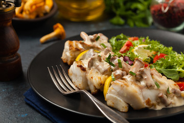 Fried cod served with mushroom sauce and salads. Portion on a black plate. Dark background.