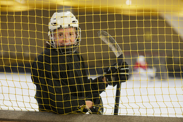Waist up portrait of female hockey player smiling at camera while standing behind gate net on rink, copy space