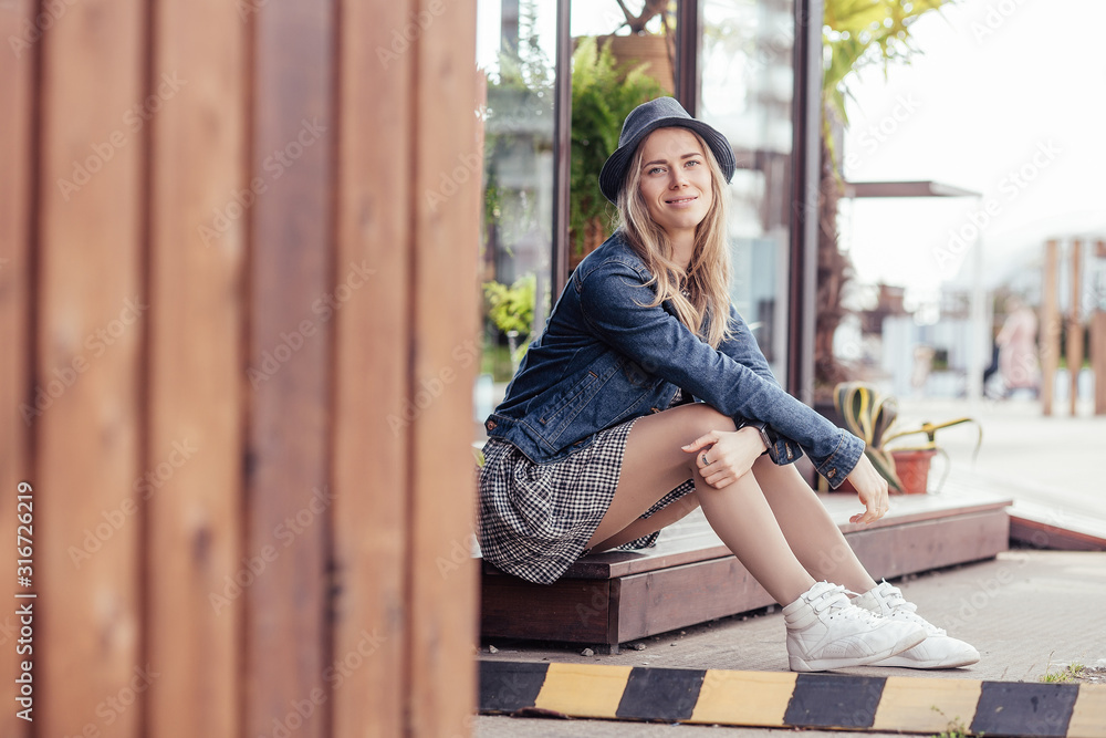 Wall mural nice young girl sits against the background of a summer cafe and basks under the first warm spring r