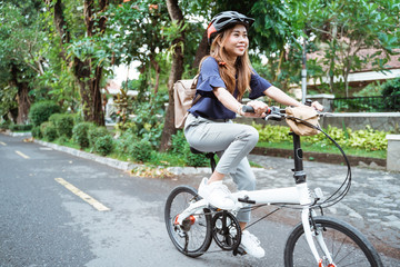 Asian young woman goes wearing a helmet and a bag riding her folding bicycle on the road