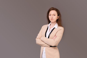Successful caucasian positive elegant businesswoman in a beige jacket with hands clasped on her chest posing on a gray background. Happy young woman advertises wholesales stores. Advertising space