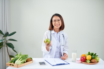 Obraz na płótnie Canvas Smiling nutritionist in her office, she is showing healthy vegetables and fruits, healthcare and diet concept.