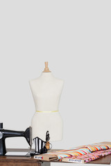 Tailor's dummy with hat and cloth pattern on sewing machine over colored background