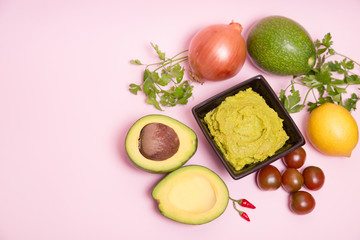 Guacamole en un bol con ingredientes sobre fondo rosa pastel.