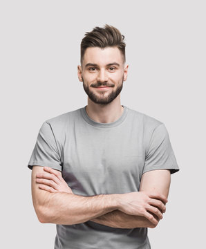 Portrait of handsome smiling young man with folded arms. Smiling joyful cheerful men with crossed hands studio shot. Isolated on gray background