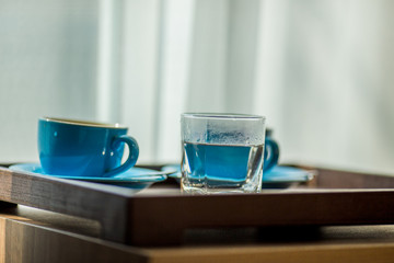 Close-up view of the blue coffee mug, clear glass for drinking water, placed on a tray to bring clear drinks, seen at resorts, hotels or bakeries