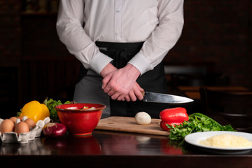 A cook with a knife stands at the table, on the table are the ingredients for breakfast.