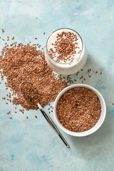 Bowl with flax seeds and glass of yogurt on color background