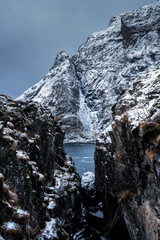 Fototapeta na wymiar Narrow cliffs and snowy mountain above a fjord. Northern Norway winter landscape photo.