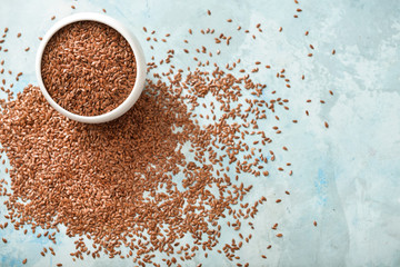 Bowl with flax seeds on color background