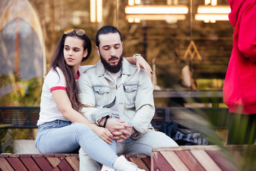 Fototapeta premium Happy romantic married couple of newlyweds gently hugging and talking making plans for the future sitting on a bench during a walk on a warm sunny day. Affectionate couple in love concept