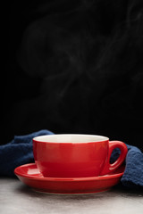Red cup of coffee with smoke and blue fabric on cement background.