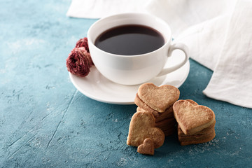 Cup of red tea with rose with homemade cookie hearts, white cloth towel on blue background