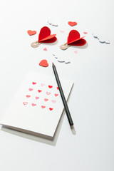 selective focus of greeting card with hearts and pencil near paper heart shaped air balloons in clouds on white background