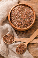 Bowl with flax seeds and spoons on wooden background